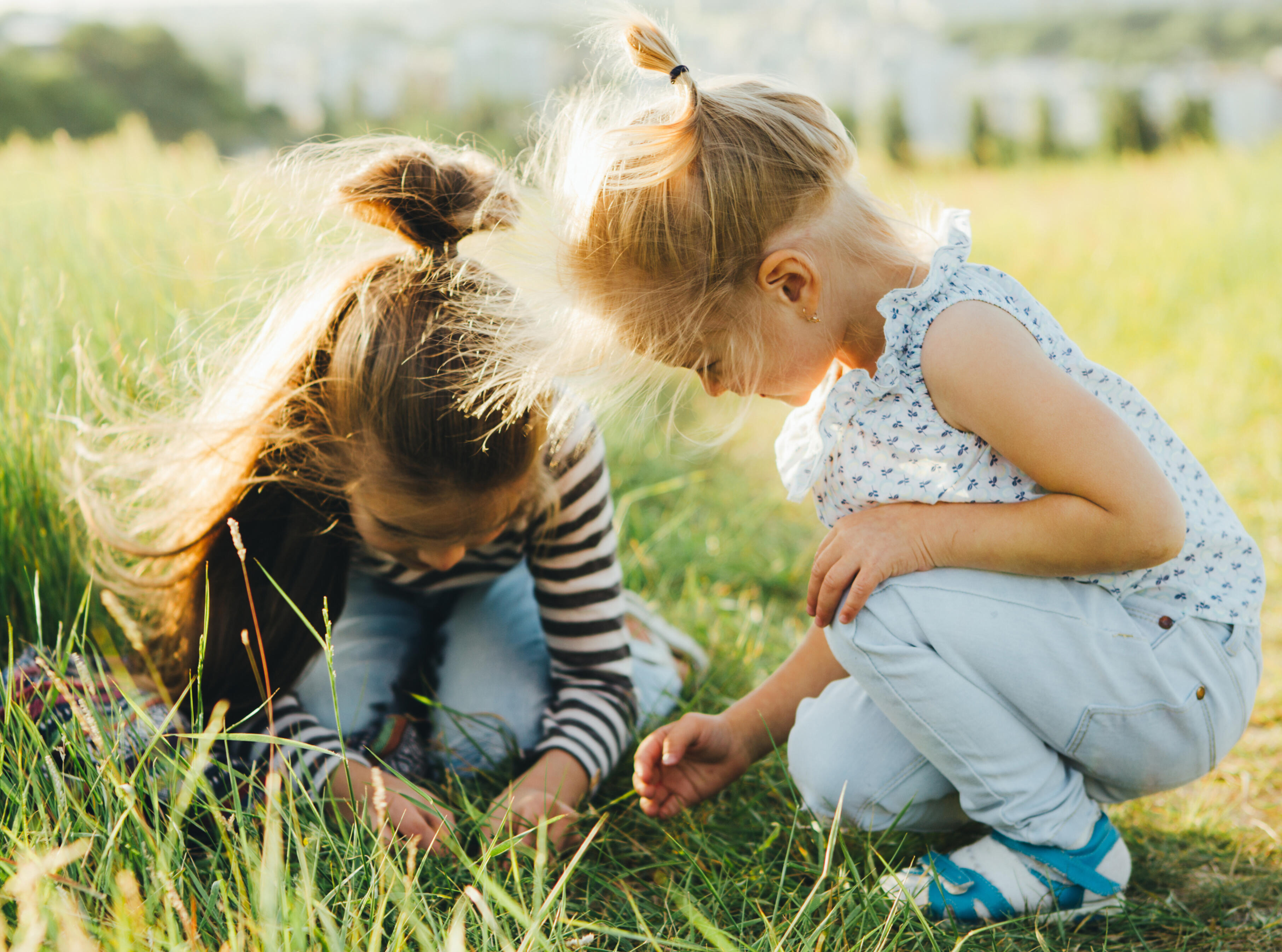 Two elementary school girls studying grass while kneeling on the grass.